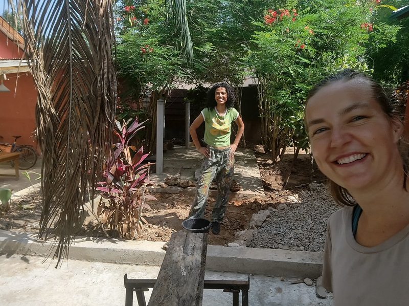 De amerikaanse vrijwilligster Aliyah en de Nederlandse Anna werken samen in de tuin. Ze maken een compostbak.